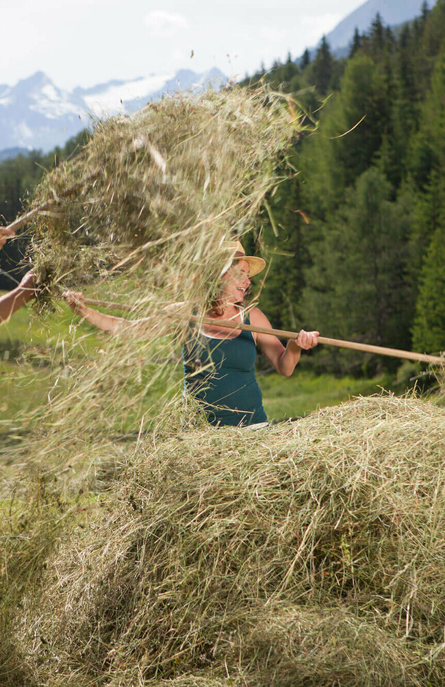 Urlaub am Bauernhof Ein Mann und eine Frau auf einer Wiese mit Heu und Heugabeln.