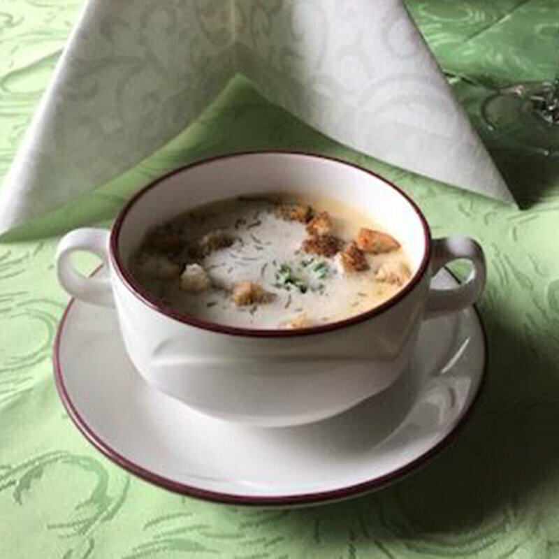 Eine Portion Knoblauchcreme-Suppe mit Croutons und Kräutern auf einem Tisch mit einer grünen Tischdecke.