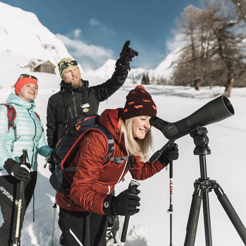 Schneeschuhwandern Ein Nationalpark Ranger zeigt zwei Frauen die Landschaft durch ein Fernglas im Koednitztal.