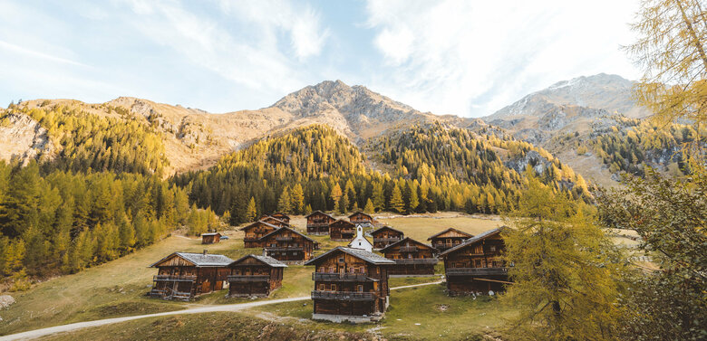 Die Hüttenansammlung mit kleiner Kapelle in der Mitte der Oberstalleralm in herbstlicher Umgebung mit verfärbten Wäldern.