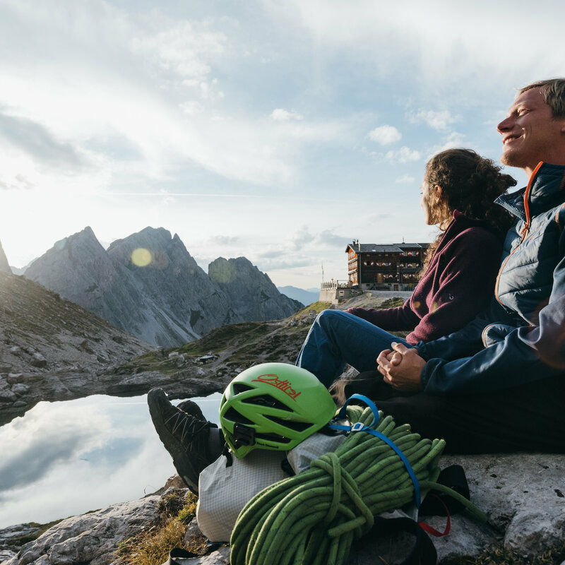 Zwei zufriedene Kletterer:innen entspannen bei der Karlsbaderhütte am Laserzsee nach erfolgreichem Aufstieg