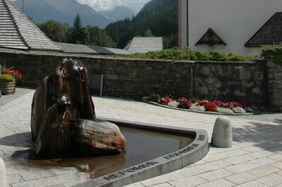 Nepomuk-Brunnen Der Nepomuk-Brunnen im Zentrum von Hopfgarten i. D., direkt neben der Pfarrkirche gelegen. Das Wasser sprudelt aus dem mehrfärbigen Stein. Im Hintergrund ist die Kirchenmauer in die davorliegende Blumenpracht an einem sonnigen Sommertag zu sehen.