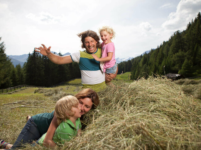 Urlaub am Bauernhof Eine Familie macht Urlaub am Bauernhof und spielt im Heu auf einer Wiese.