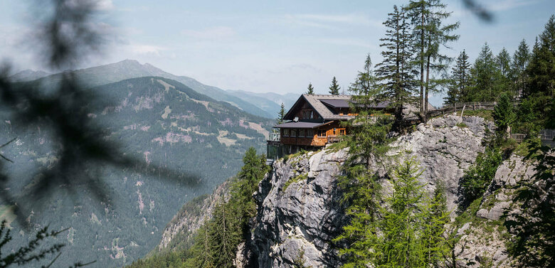 Blick auf die am Felsrand liegende Dolomitenhütte an einem sonnigen Tag