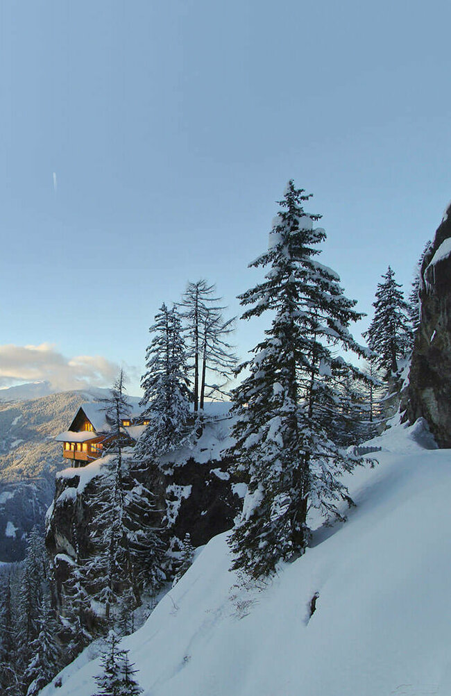 Panoramablick auf die beleuchtete Dolomitenhütte im Winter. Die Landschaft ist tief verschneit.