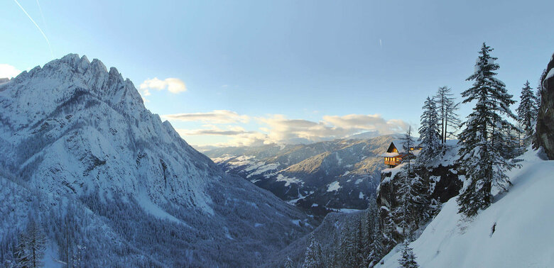 Panoramablick auf die beleuchtete Dolomitenhütte im Winter. Die Landschaft ist tief verschneit.