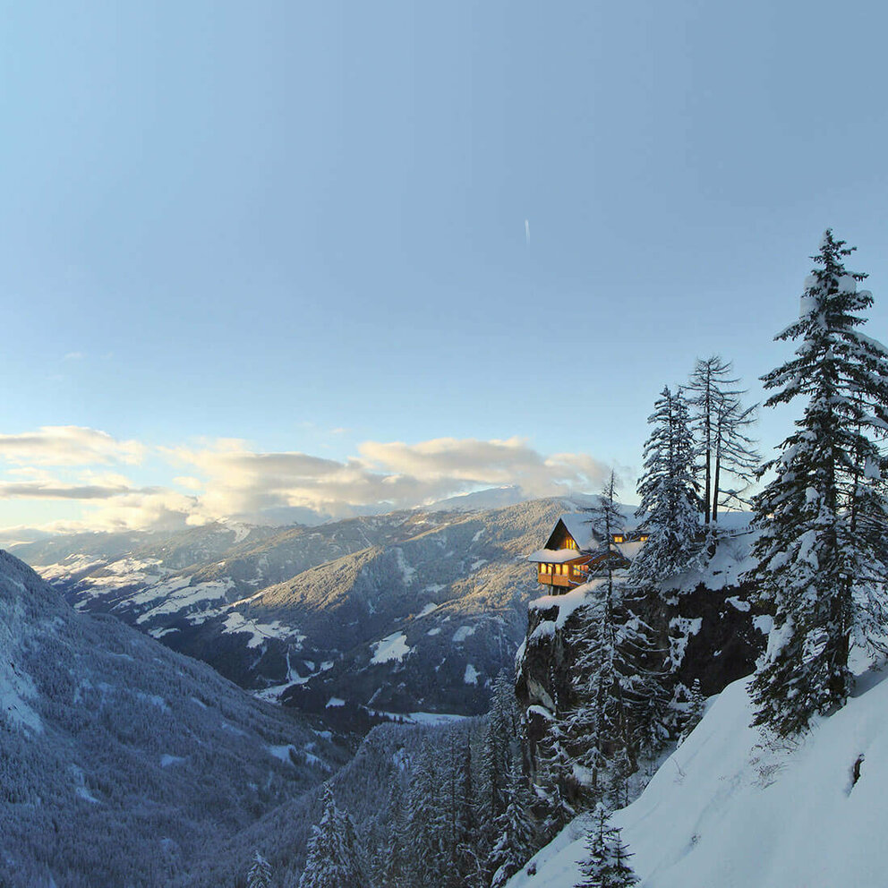 Panoramablick auf die beleuchtete Dolomitenhütte im Winter. Die Landschaft ist tief verschneit.