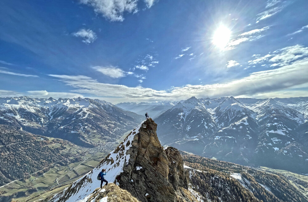 Spitzer Berggipfel mit einigen Schneefeldern bei herrlichem Frühlingswetter mit Bergpanorama im Hintergrund.