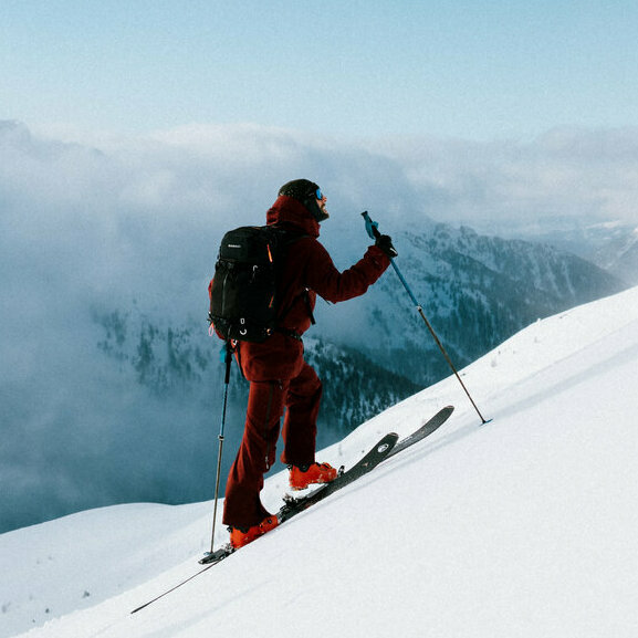Zwei Skitourensportler erklimmen im Gleichschritt auf ihren Tourenskiern einen mittelsteilen Berghang an einem Schönwettermorgen. Dahinter verdeckt zäher Hochnebel einen Teil der Berge.