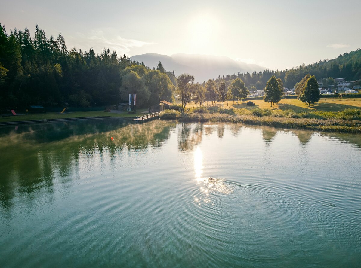Eine Person schwimmt in der Morgensonne durch den menschenleeren Tristacher See.