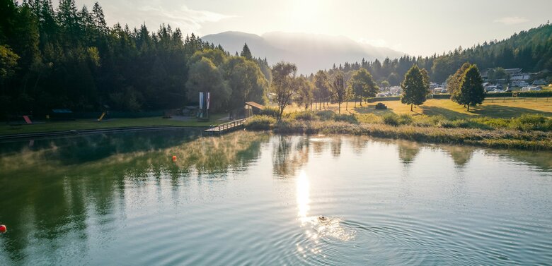 Eine Person schwimmt in der Morgensonne durch den menschenleeren Tristacher See.