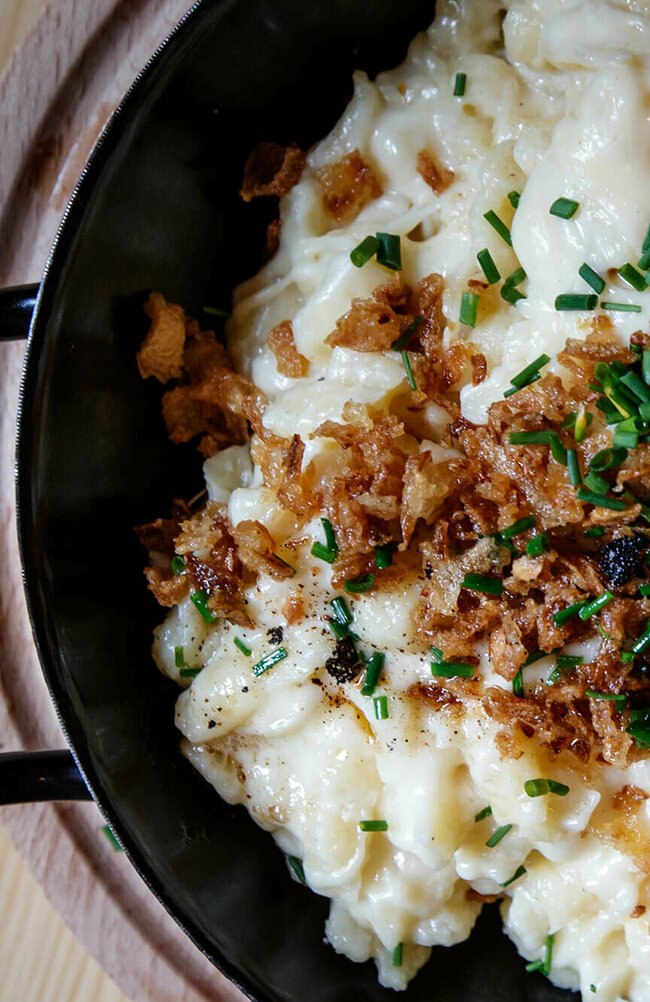 Kaesespatzle Käsespätzle mit gerösteten Zwiebeln traditionell in einem kleinen, schwarzen Eisenpfännchen