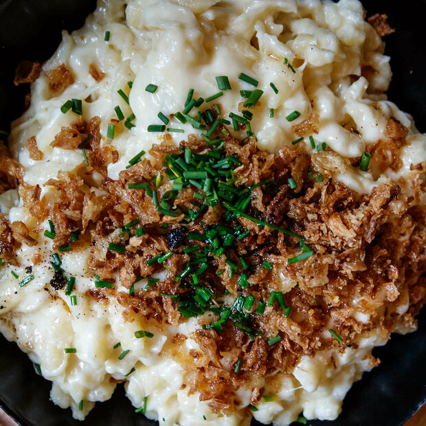 Kaesespatzle Käsespätzle mit gerösteten Zwiebeln traditionell in einem kleinen, schwarzen Eisenpfännchen