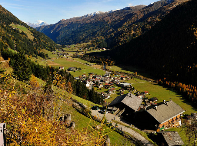 Herbstbild von St. Jakob im Defereggental, von oben fotografiert mit Blick ins Tal dahinter, bei bestem Wetter.