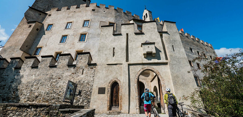 Biken Schloss Bruck Zwei Biker schieben ihre Räder durch einen steinernen Bogen am Eingang des Schloss Bruck in Lienz.