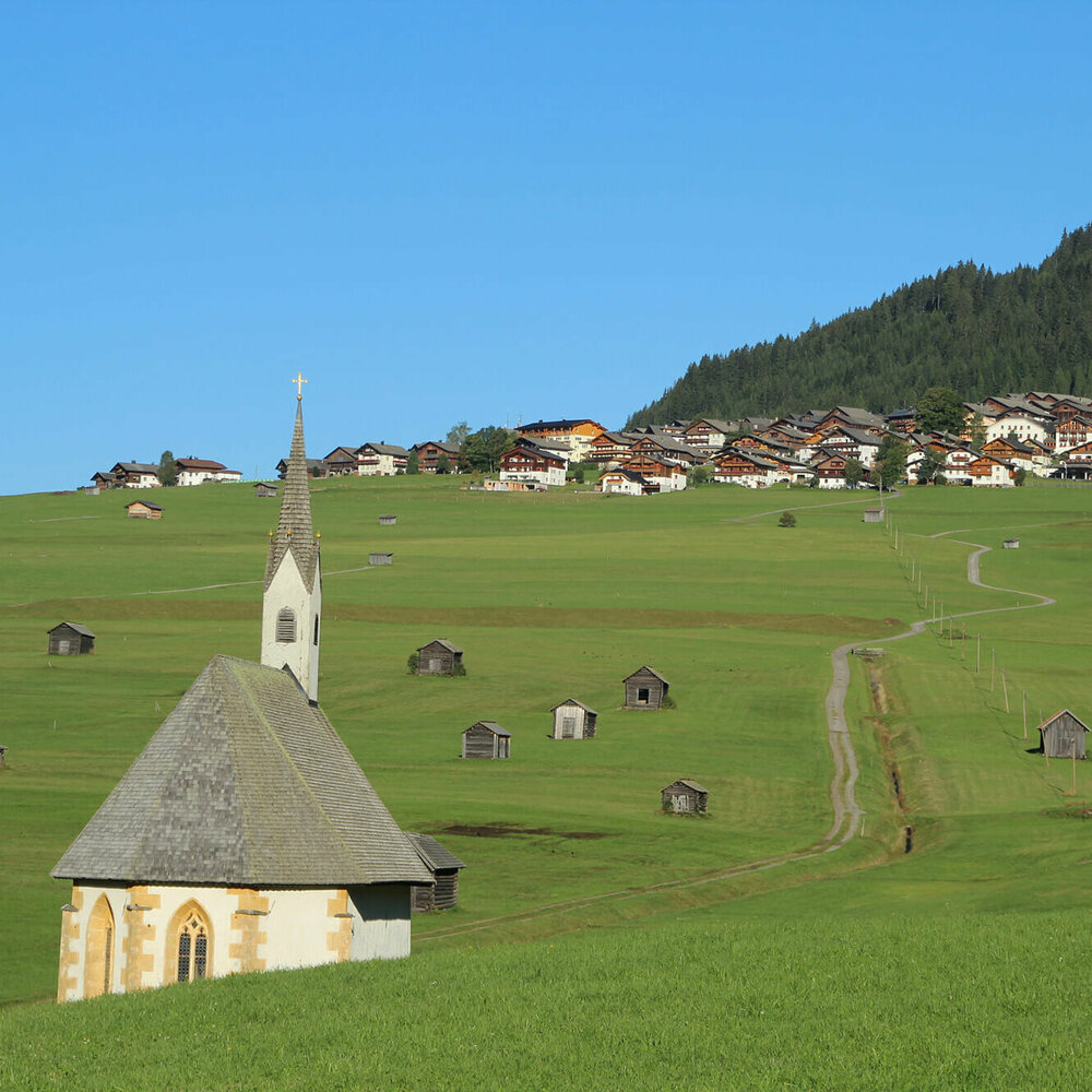 Blick von den Tilliacher Mösern auf das Dorf mit den saftig grünen Wiesen. Zwischen den unzähligen kleinen Heustadeln die 2 Kapellen St. Nikolaus und St. Helena.