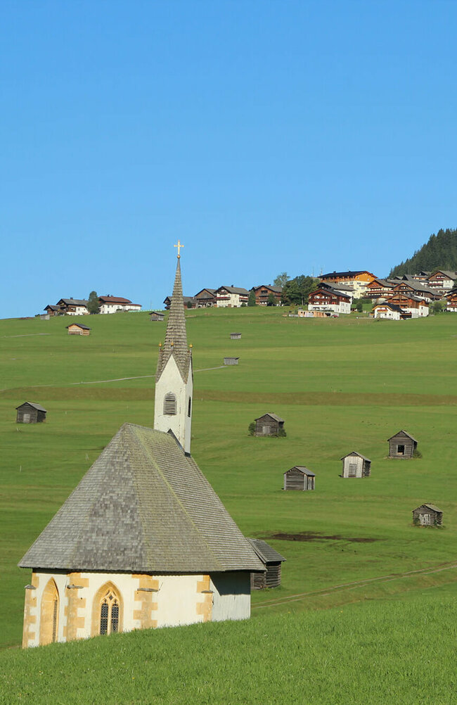 Blick von den Tilliacher Mösern auf das Dorf mit den saftig grünen Wiesen. Zwischen den unzähligen kleinen Heustadeln die 2 Kapellen St. Nikolaus und St. Helena.