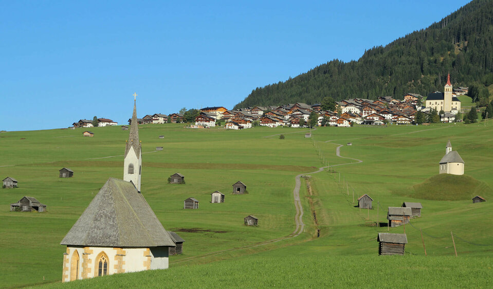 Blick von den Tilliacher Mösern auf das Dorf mit den saftig grünen Wiesen. Zwischen den unzähligen kleinen Heustadeln die 2 Kapellen St. Nikolaus und St. Helena.