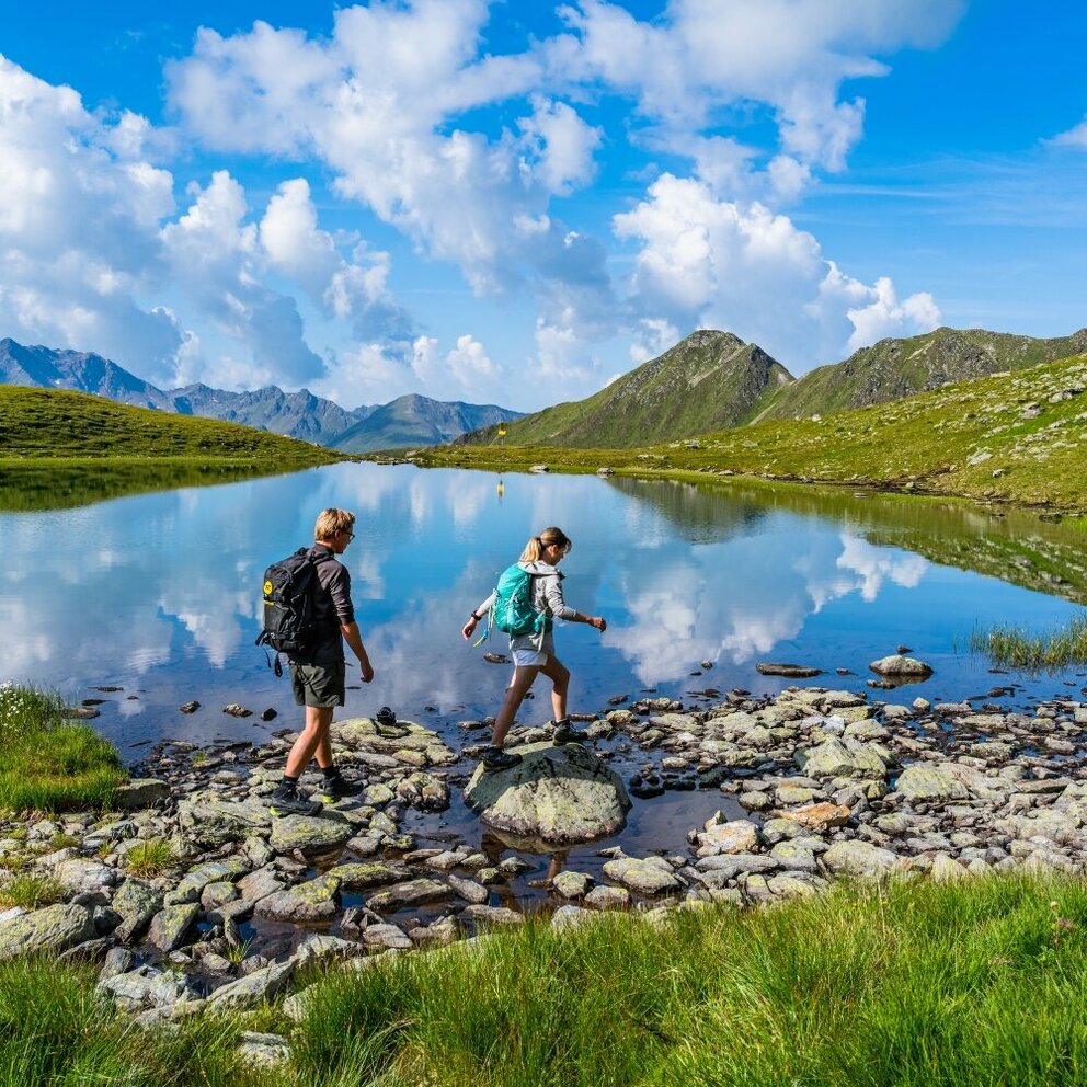 Ein Pärchen steigt über einige Steine am Gritzer See in St.Veit im Defereggen an einem herrlichen Sommertag.