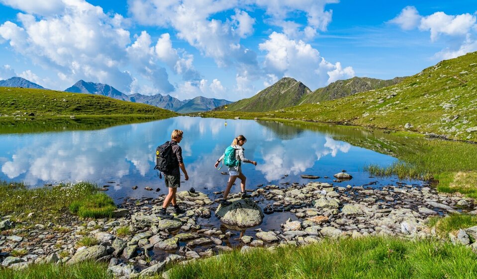 Ein Pärchen steigt über einige Steine am Gritzer See in St.Veit im Defereggen an einem herrlichen Sommertag.