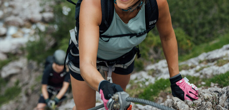 Zwei Frauen klettern am Klettersteig namens "Verborgene Welt" am Fels nach oben.
