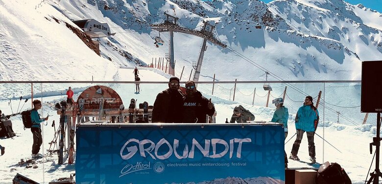 Ground it Zwei Erwachsene hinter einer Art Theke beim Ground it Festival auf einer Sonnenterrasse in einem Skigebiet.