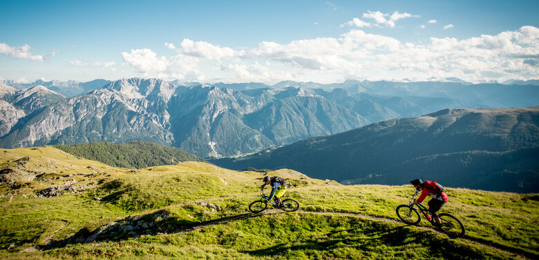 Zwei Radfahrer auf einem schmalen Trail mit einzigartigem Bergpanorama.