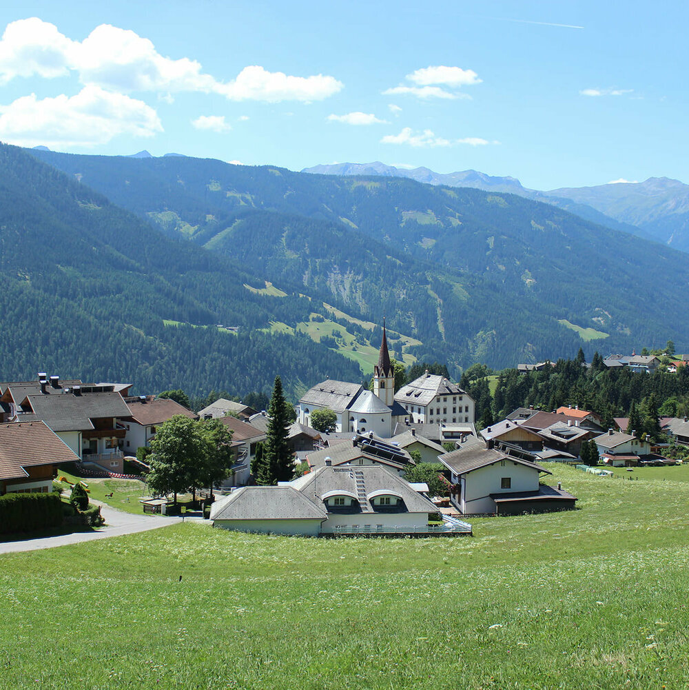 Anras Blick auf Anras mit einem grünem Feld im Vordergrund und bewaldeten Berghängen im Hintergrund.