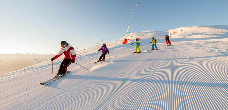 Ein Skilehrer fährt mit mehreren Kindern über eine frisch präparierte Abfahrt im Skigebiet Zettersfeld.