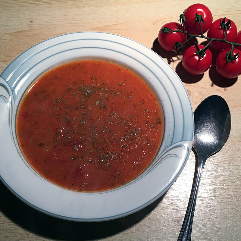Ein Teller mit Tomatensuppe und einem Löffel und mehreren Kirschtomaten daneben.