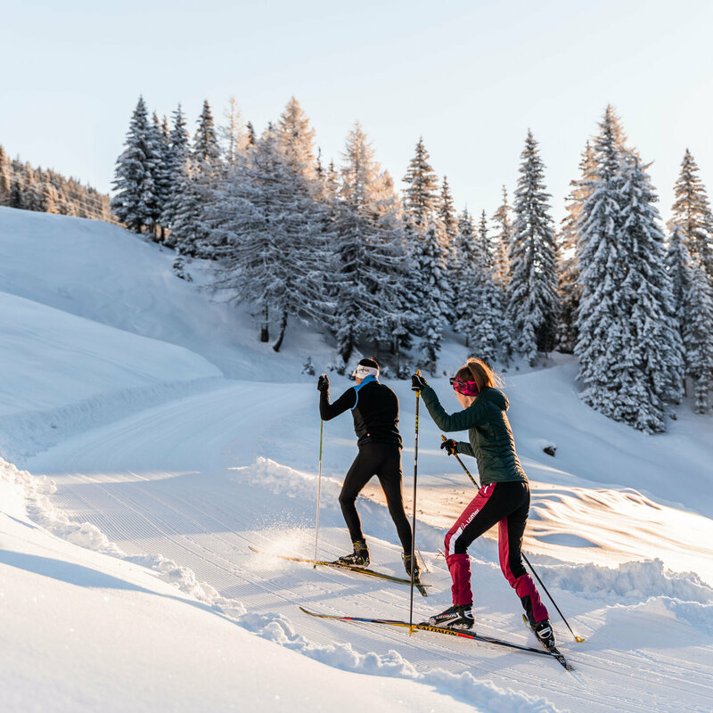 Zwei Langläufer:innen im Aufstieg durch die Winterlandschaft