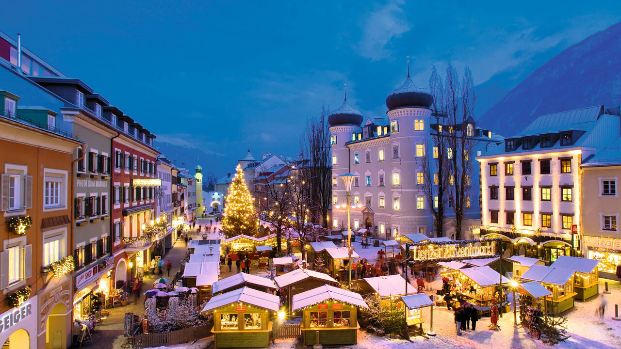 Aufnahme vom Lienzer Adventmarkt am Hauptplatz bei Nacht. Die Hütten und ein großer Tannenbaum in der Mitte sind beleuchtet.