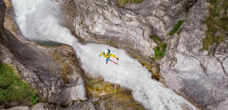 Eine Frau mit gelber Jacke geht über eine luftige Seilbrücke über den Fluss in der Galitzenklamm.