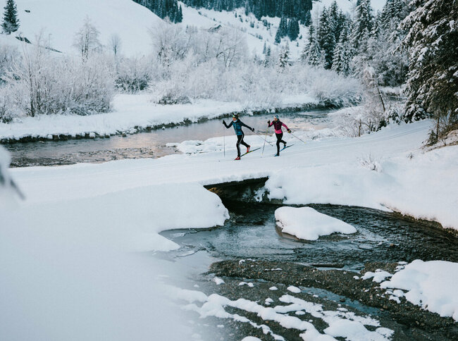 Zwei Langläufer:innen laufen am Gewässer vorbei in Innervillgraten