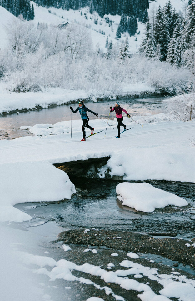 Zwei Langläufer:innen laufen am Gewässer vorbei in Innervillgraten