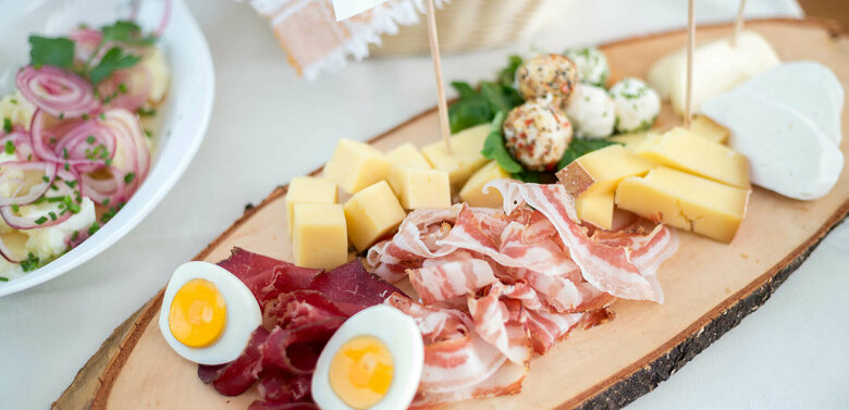 Brettljause mit verschiedenen Käsesorten in Würfel geschnitten, feinen Speck- und Henkelescheiben und hartgekochten Eiern.
