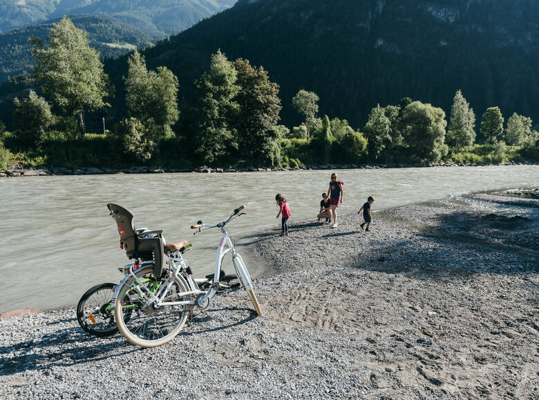 Radfahren Eine Familie spielt am Ufer der Isel, im Vordergrund stehen zwei Räder eines in weiß und ein Kinderrad in giftgrün