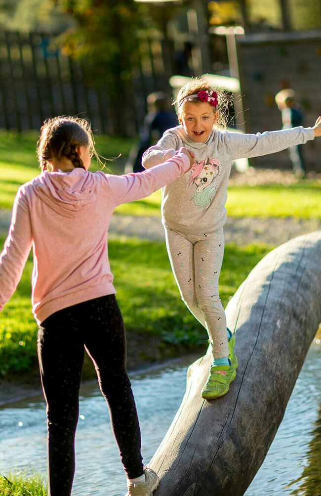 Zwei Mädchen spielen auf einem Holzstamm über Wasser auf dem Spielplatz in der Galitzenklamm.
