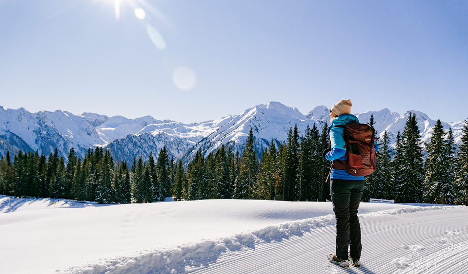 Eine Frau wandert am Dorfberg im Winterwanderdorf Kartitsch und genießt die Aussicht auf den Karnischen Kamm.