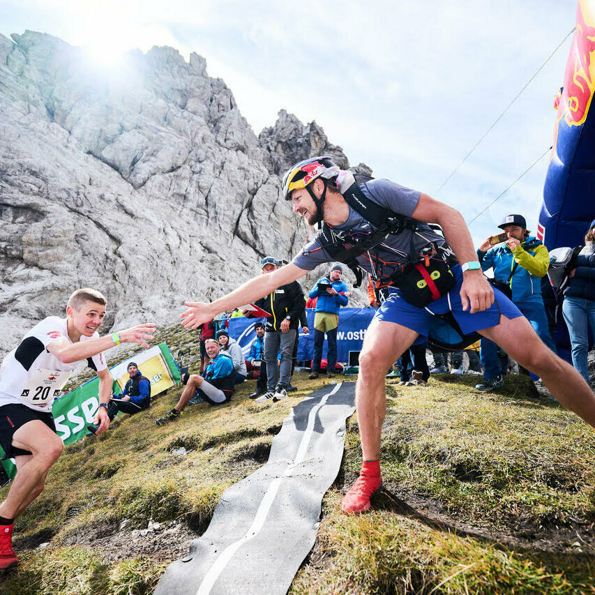 Der Dolomitenlauf ist ein Hochleistungs-Teambewerb, auf dem Foto sieht man den Bergläufer, der am Übergabepunkt ankommt und den Paragleiter abklatscht.