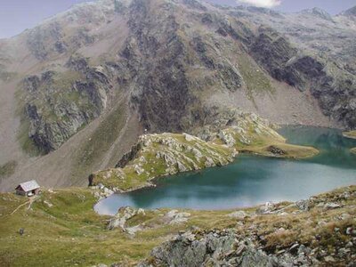 Geigensee Der Blick von etwas oberhalb auf den Geigensee in Hopfgarten i. D., der seinen Namen seiner geigenförmigen Form zu verdanken hat. Das blaue Wasser hebt sich eindeutig von der grün-grauen, felsigen Umgebung ab. Links vom See steht eine kleine Hütte.