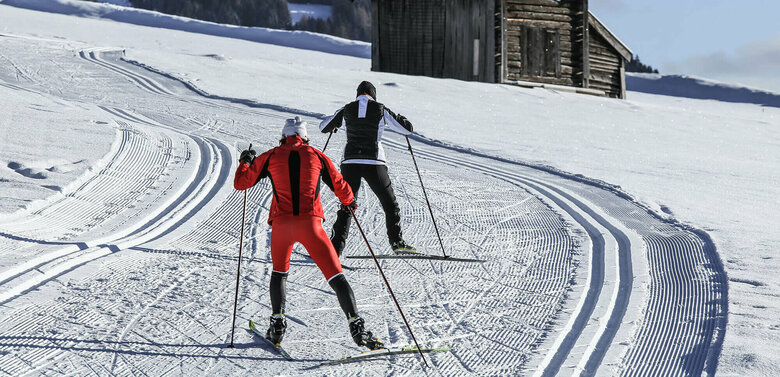 Langlauf Granzlandloipe Zwei Langläufer:innen auf der Grenzlandloipe vorbei an einer kleinen Hütte aus Holz
