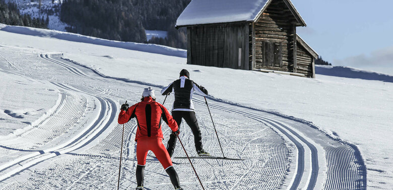 Langlauf Granzlandloipe Zwei Langläufer:innen auf der Grenzlandloipe vorbei an einer kleinen Hütte aus Holz