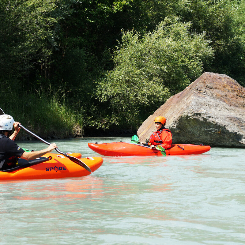 Drei Kajakfahrer in rot-orangenen Kajaks fahren auf der Isel in ruhigem Gewässer.
