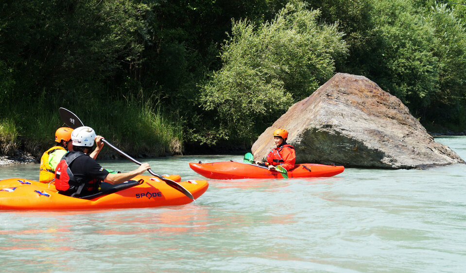 Drei Kajakfahrer in rot-orangenen Kajaks fahren auf der Isel in ruhigem Gewässer.