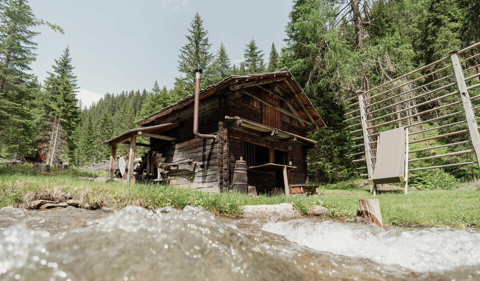 Sommeraufnahme der Mühle im Freilichtmuseum Alpines Leben in Innervillgraten, im Vordergrund fließt ein klarer Bach