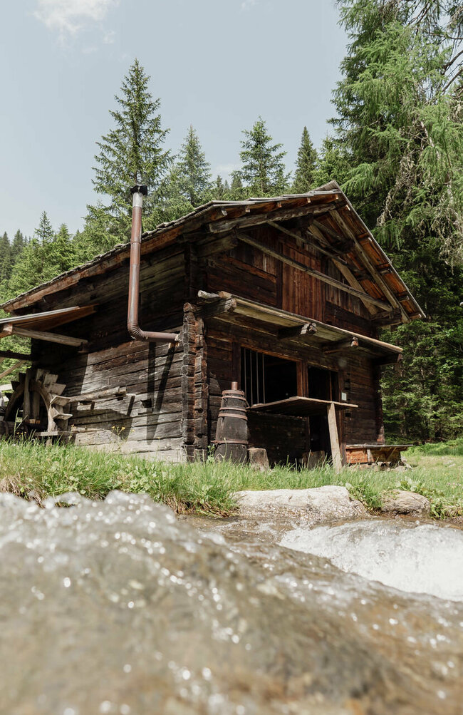 Lodenstampf Sommeraufnahme der Mühle im Freilichtmuseum Alpines Leben in Innervillgraten, im Vordergrund fließt ein klarer Bach