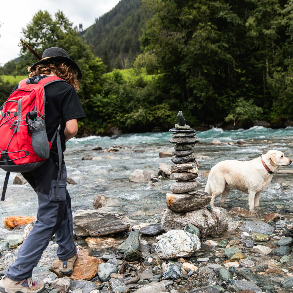 Ein Kind mit einem roten Rucksack wandert mit einem Hund am Iseltrail.