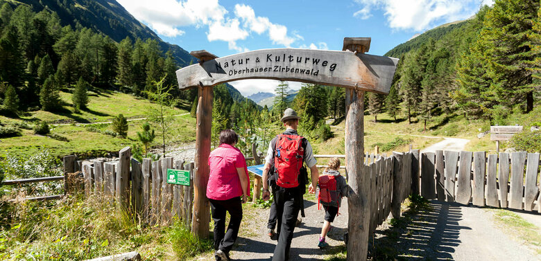 Oberhauser Zirbenwald Eine Familie in Wanderkleidung geht durch das aus Holz gebaute Eingangstor am Oberhauser Zirbenwald.