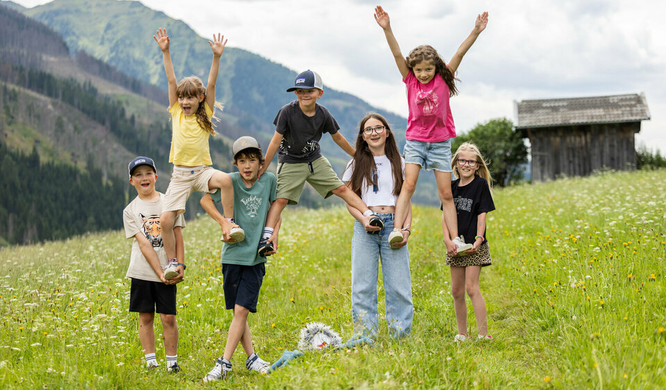 Kinder laufen über eine Wiese und heben zwei Kinder in die Höhe